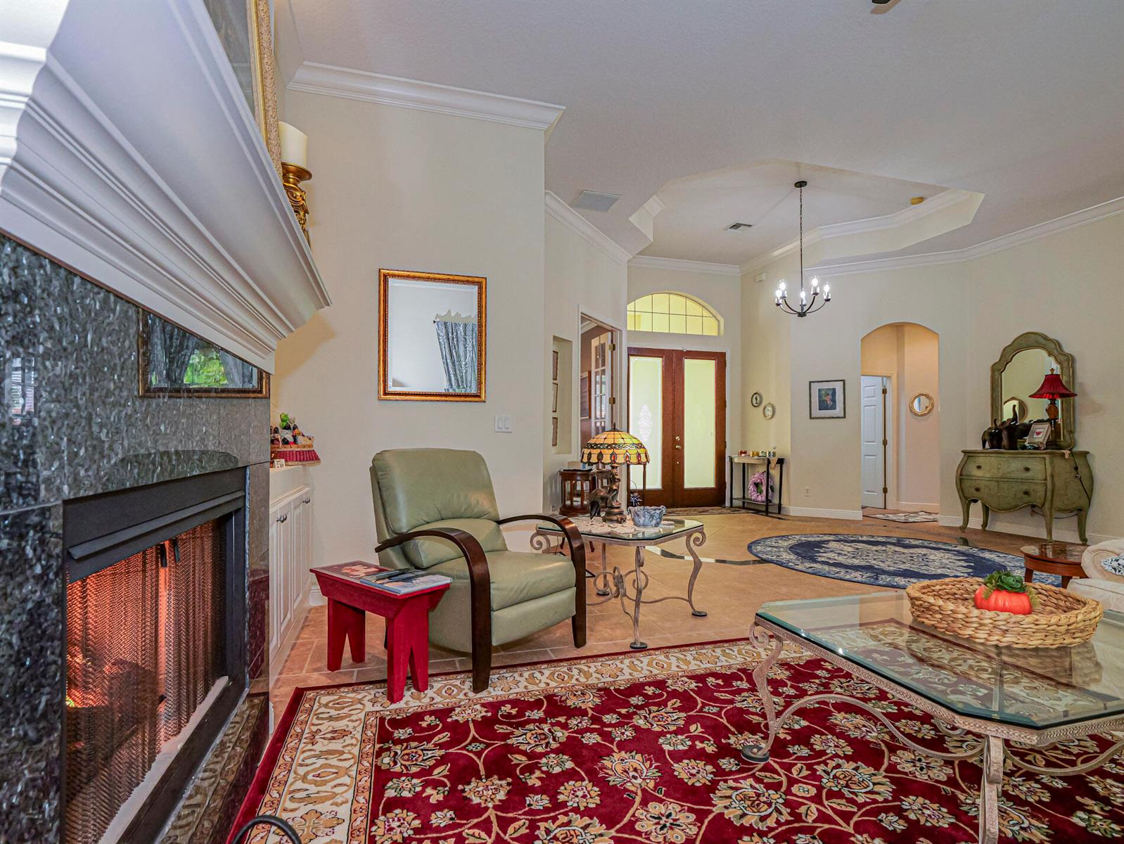 A living room features a fireplace, a green armchair, and a red patterned area rug — 5873 Pine Ridge Circle, Vero Beach FL 32967, VERO BEACH, FL