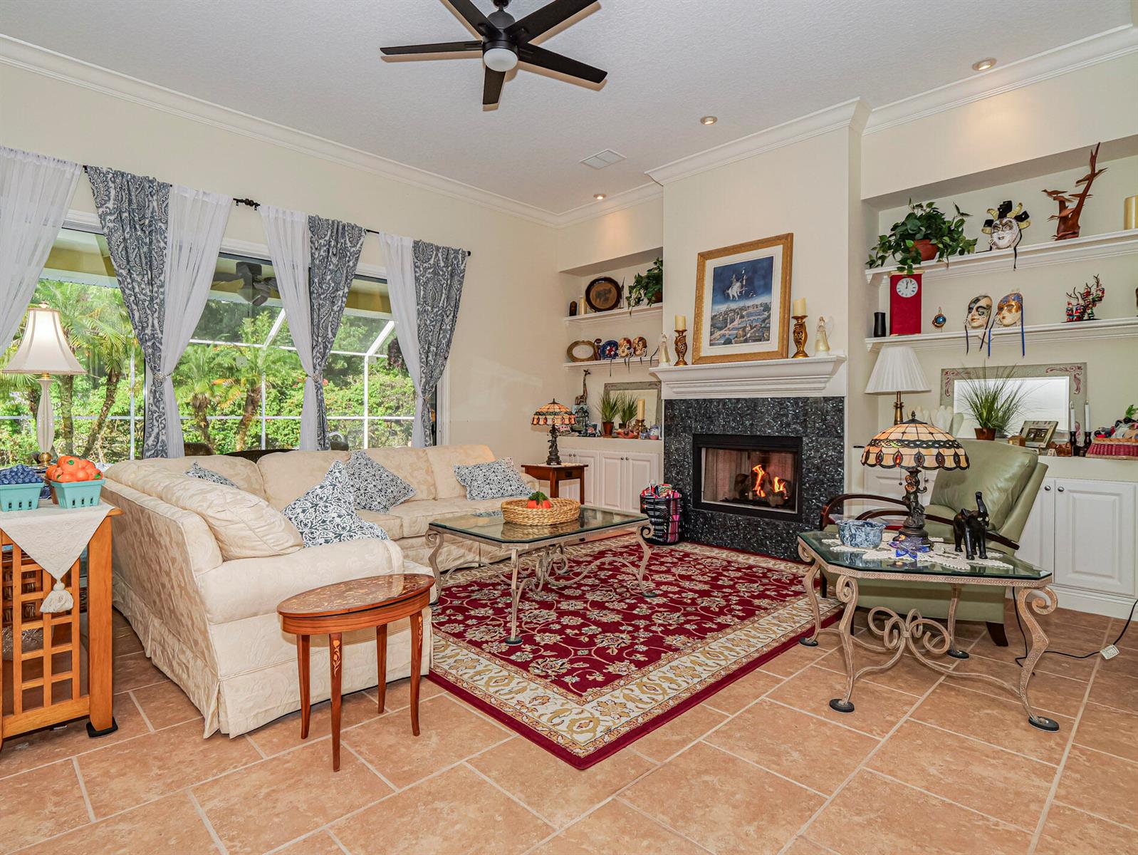 A living room features a fireplace, a red patterned rug, and large windows with curtains — 5873 Pine Ridge Circle, Vero Beach FL 32967, VERO BEACH, FL
