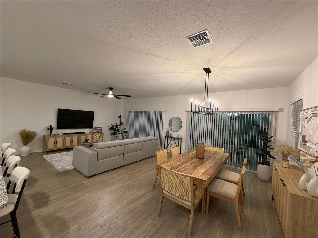 An open-concept living and dining area features light wood-look flooring, neutral furniture, and a chandelier — 1814 NW 248TH WAY, NEWBERRY, FL