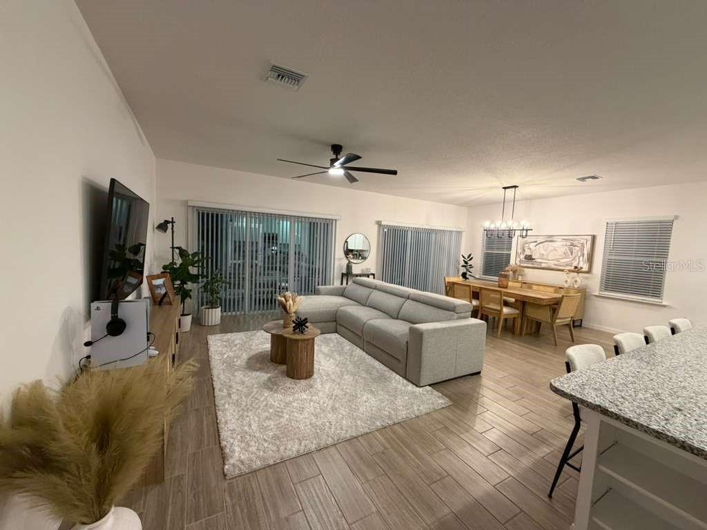 An open-concept living and dining area features tile flooring, a sectional sofa, and neutral decor — 1814 NW 248TH WAY, NEWBERRY, FL