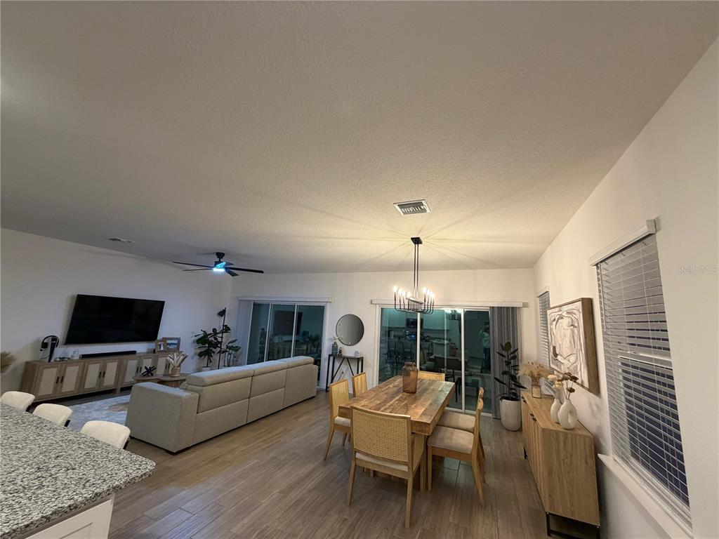An open-concept living and dining area features light wood flooring, a neutral sofa, and chandelier — 1814 NW 248TH WAY, NEWBERRY, FL