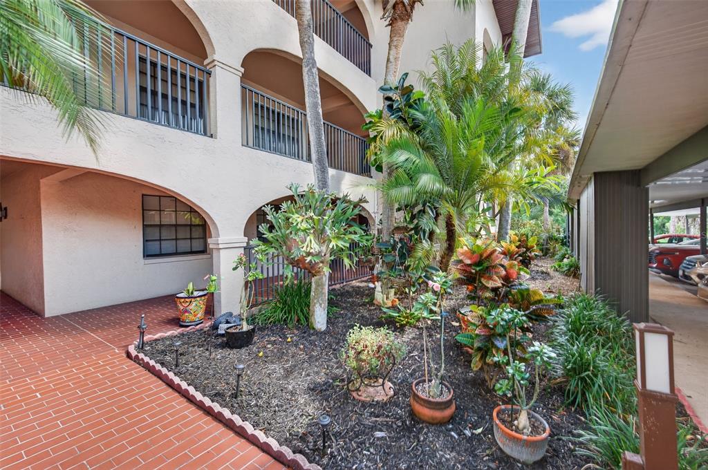 A ground-level view of a building exterior with a brick walkway and landscaped garden area — 23465 HARBORVIEW ROAD UNIT 814, PUNTA GORDA, FL