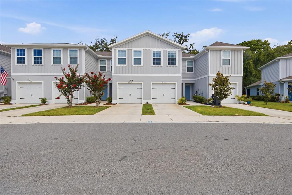 A row of light gray two-story townhomes with white garage doors and green lawns — 12126 GRIZZLY LANE, NEW PORT RICHEY, FL