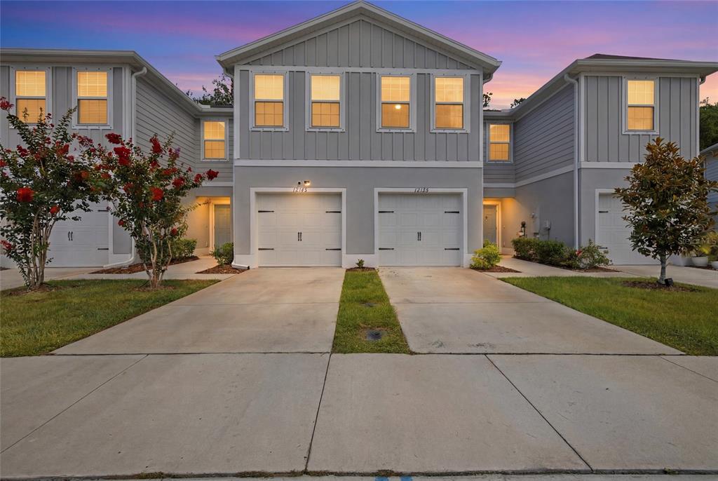 A multi-unit residential building exterior features gray siding, white garage doors, and concrete driveways — 12126 GRIZZLY LANE, NEW PORT RICHEY, FL