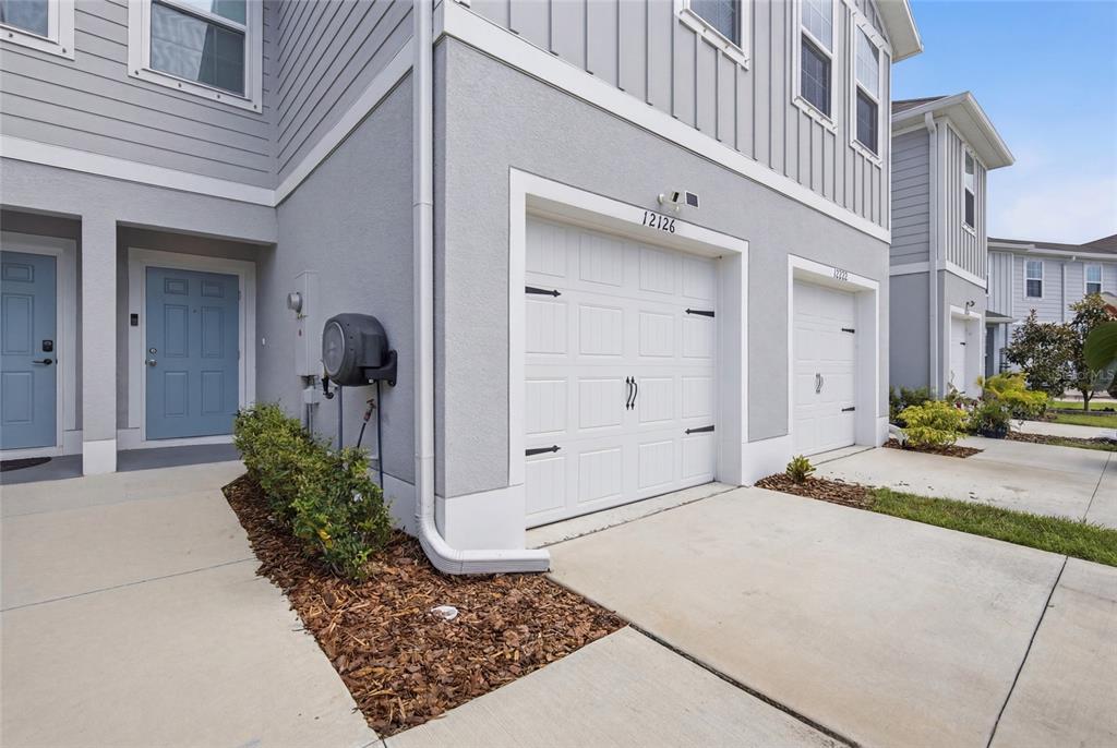 A two-story gray townhouse exterior features a white garage door and a blue front door — 12126 GRIZZLY LANE, NEW PORT RICHEY, FL