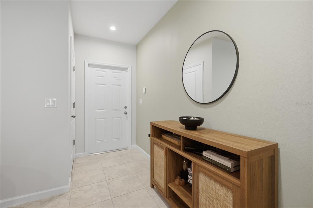 An entryway features a white door, tile flooring, a wooden console table, and a round mirror — 12126 GRIZZLY LANE, NEW PORT RICHEY, FL