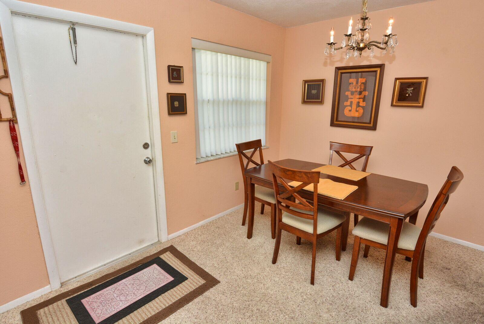 A dining area features a wooden table with four chairs, a chandelier, and beige carpeting — 1225 NW 21st Street # 2010, Stuart FL 34994, STUART, FL