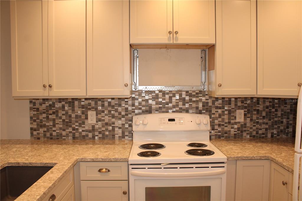 A kitchen features white cabinets, a mosaic tile backsplash, and a white electric range — 3602 54TH STREET W UNIT D1, BRADENTON, FL