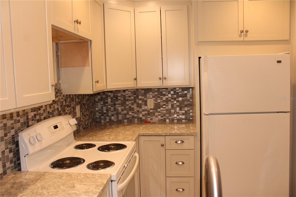 A kitchen features white cabinets, a mosaic tile backsplash, a white stove, and a refrigerator — 3602 54TH STREET W UNIT D1, BRADENTON, FL