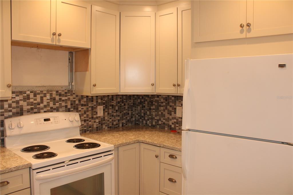 A kitchen features white cabinets, a mosaic tile backsplash, a white stove, and a refrigerator — 3602 54TH STREET W UNIT D1, BRADENTON, FL