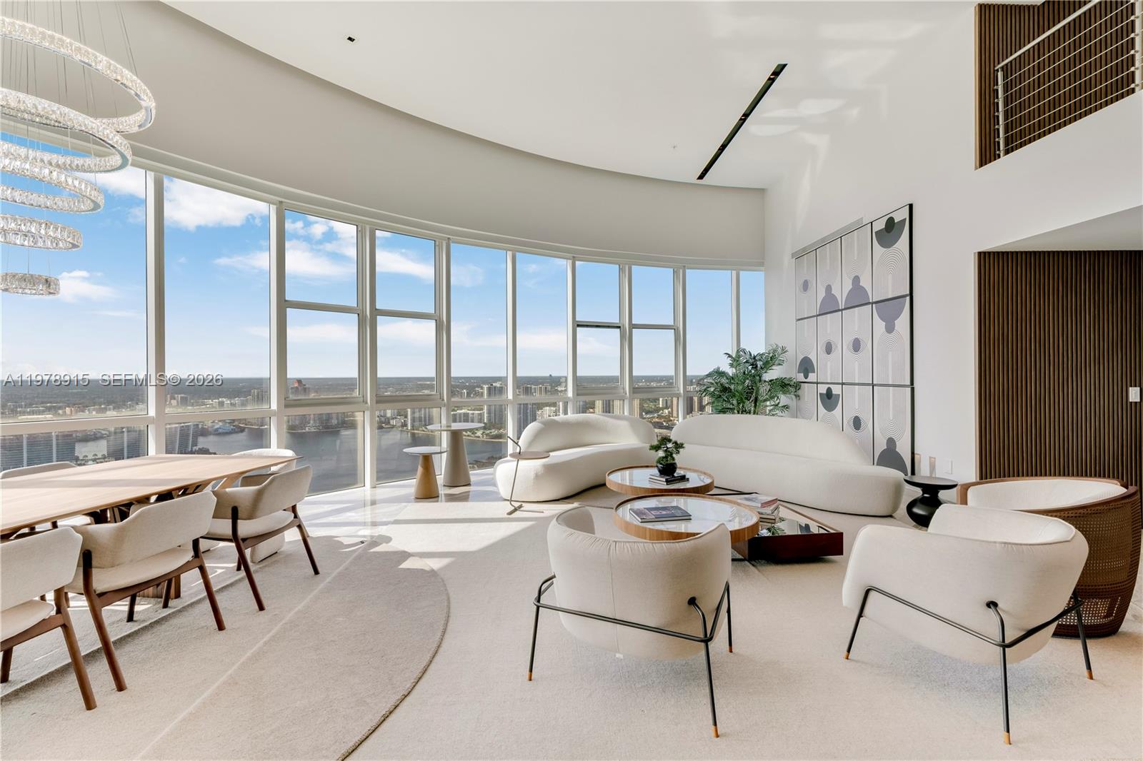 A bright, modern living and dining area features floor-to-ceiling curved windows with city views — 18201 E Collins Ave, Sunny Isles Beach FL 33160, SUNNY ISLES BEACH, FL