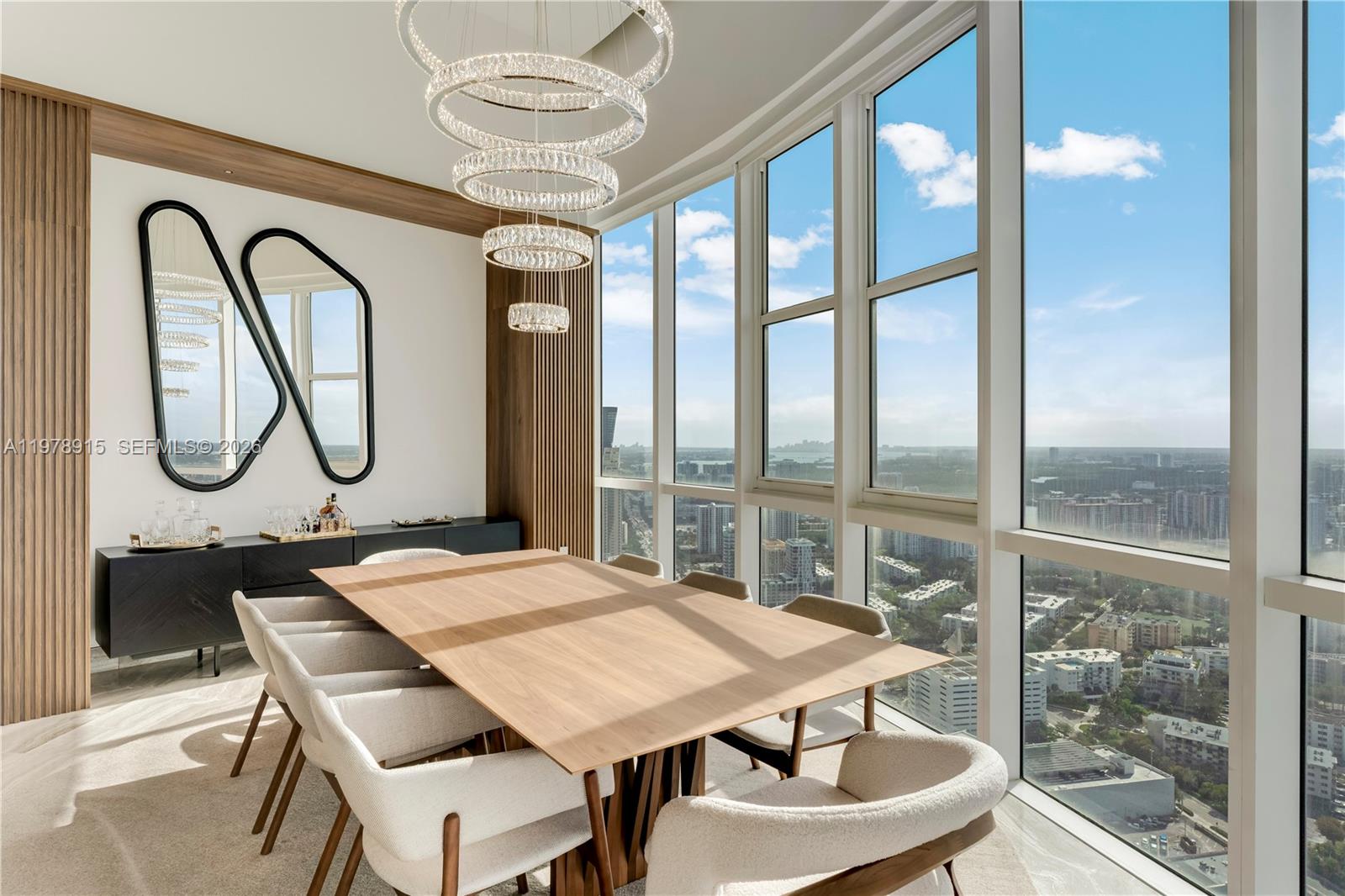 A dining room features a wooden table, modern chairs, a tiered chandelier, and floor-to-ceiling windows — 18201 E Collins Ave, Sunny Isles Beach FL 33160, SUNNY ISLES BEACH, FL