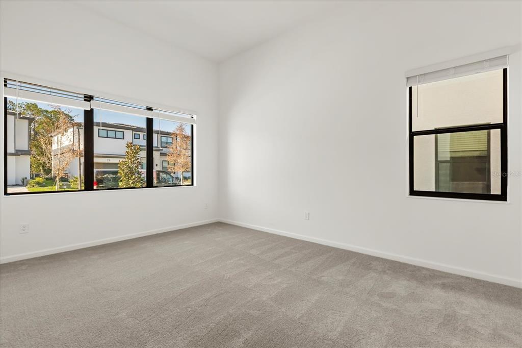 An empty bedroom features white walls, gray carpeting, and large windows with black frames — 11073 MORAY BAY AVE, ORLANDO, FL