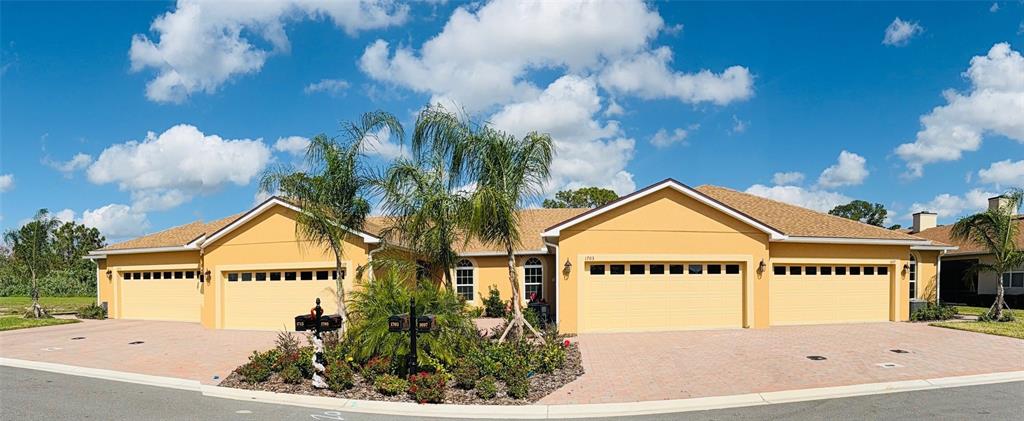 A wide-angle exterior view of a yellow residential building with multiple garage doors and palm trees — 1703 LINZ COURT, WINTER HAVEN, FL