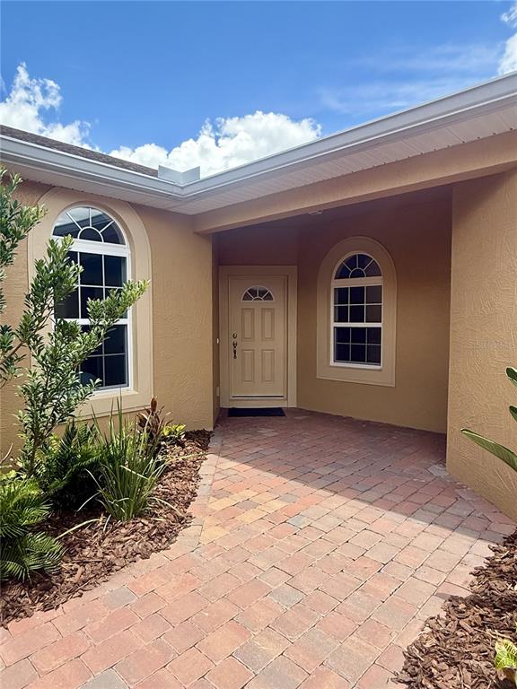 A tan house exterior features a brick paver walkway leading to a front entrance door — 1703 LINZ COURT, WINTER HAVEN, FL
