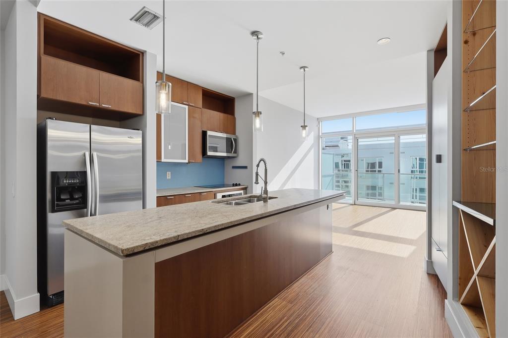 A modern kitchen features a granite-topped island, wood cabinetry, stainless steel appliances, and balcony access — 111 N 12TH STREET UNIT 1811, TAMPA, FL
