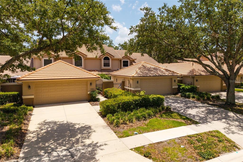 The exterior of a multi-unit residential building features tan stucco walls, tile roofs, and driveways — 17557 FAIRMEADOW DRIVE, TAMPA, FL