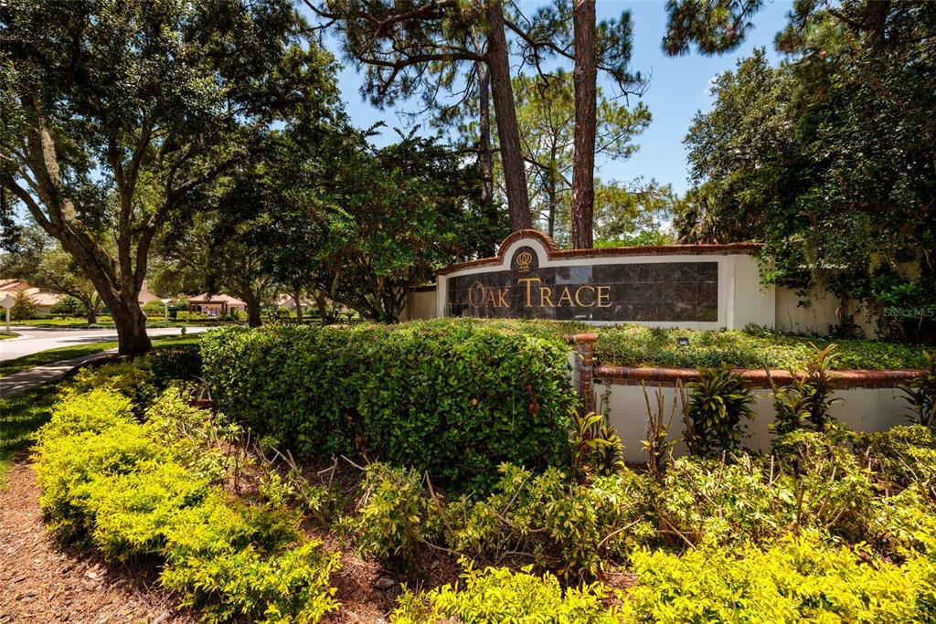 A stone monument sign reading Oak Trace stands behind manicured hedges and mature trees — 17557 FAIRMEADOW DRIVE, TAMPA, FL