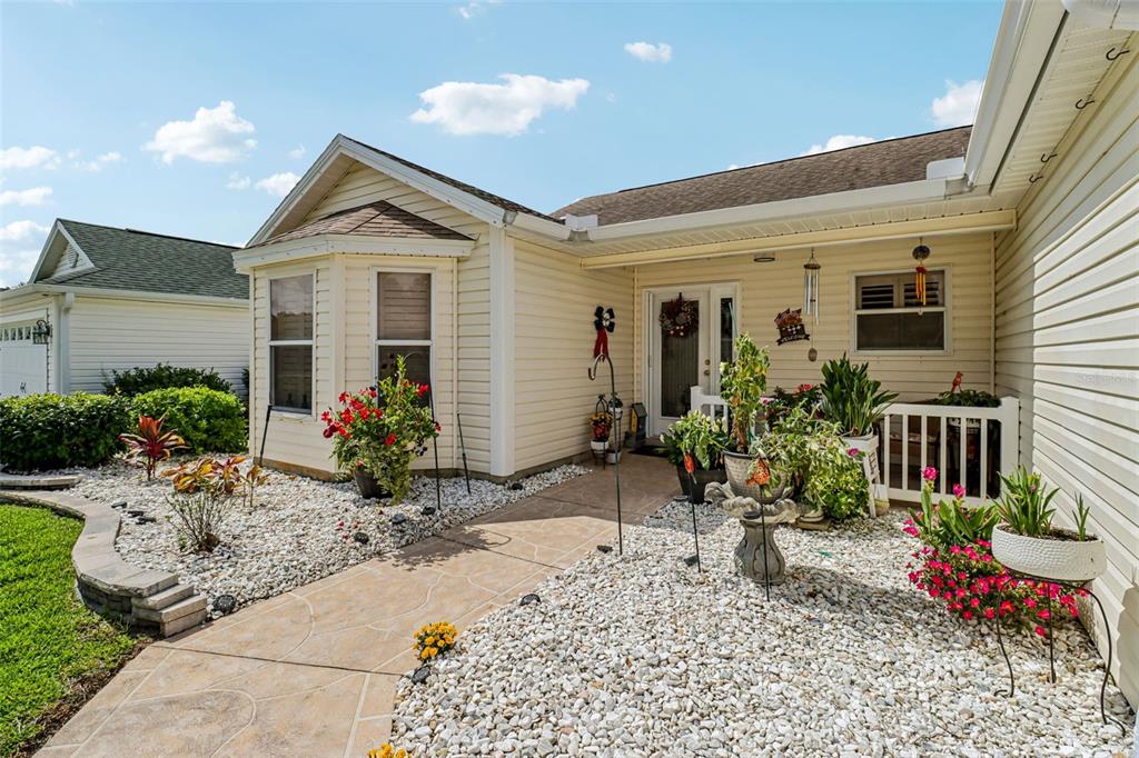 A covered front porch features light siding, a white door, and several potted plants — 16581 SE 77TH NORTHRIDGE COURT, THE VILLAGES, FL