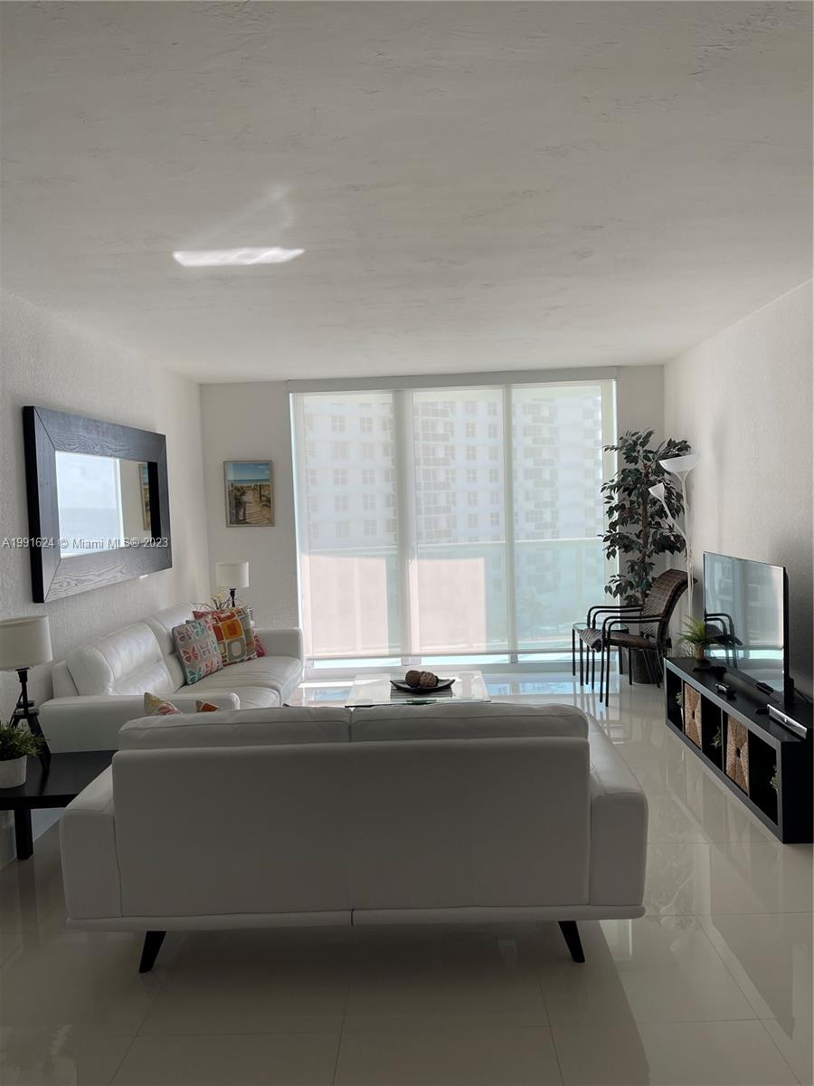 A living room features white sofas, a black media console, and large windows with blinds — 3801 S OCEAN DR # 7X, Hollywood FL 33019, HOLLYWOOD, FL