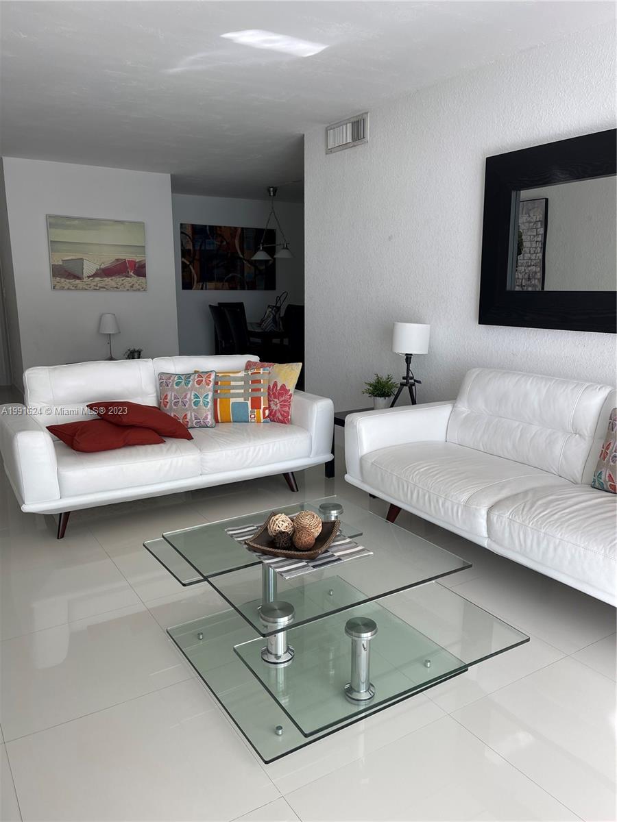 A living room features two white leather sofas, a glass coffee table, and white tile floors — 3801 S OCEAN DR # 7X, Hollywood FL 33019, HOLLYWOOD, FL
