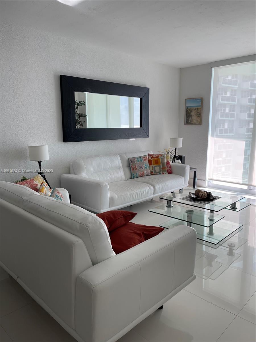A living room features two white leather sofas, a glass coffee table, and a large mirror — 3801 S OCEAN DR # 7X, Hollywood FL 33019, HOLLYWOOD, FL