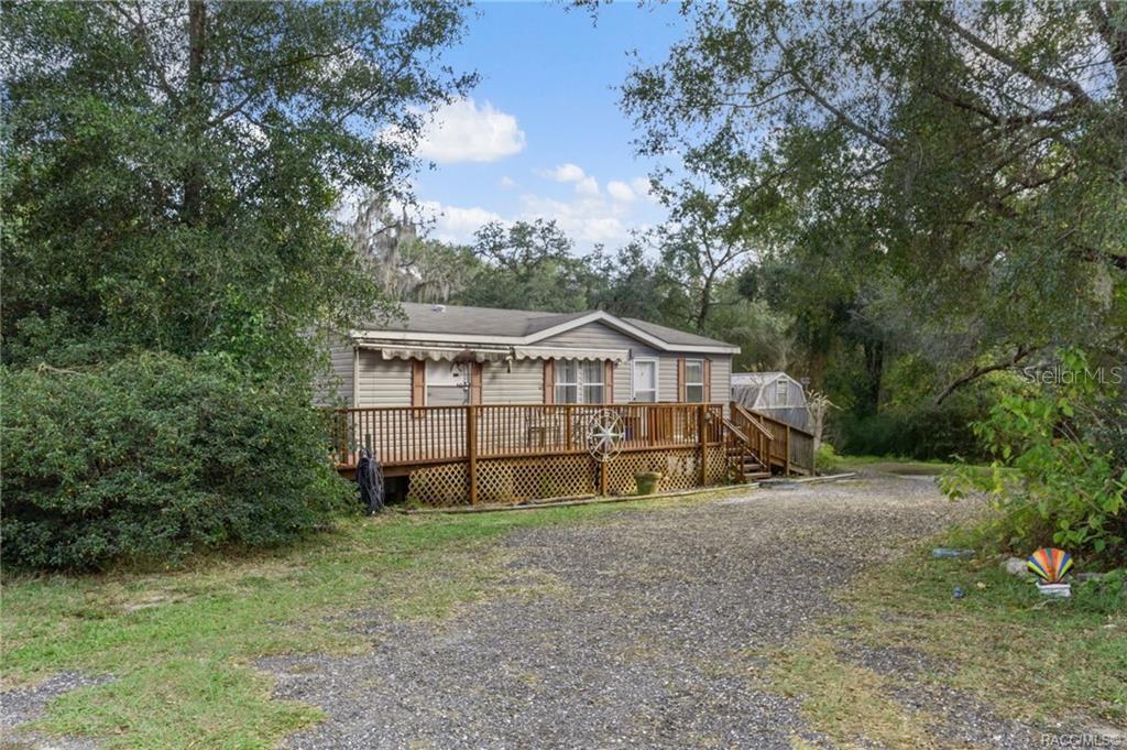 A single-story manufactured home with a wooden deck sits on a gravel driveway — 16362 CHEROKEE ROAD, BROOKSVILLE, FL