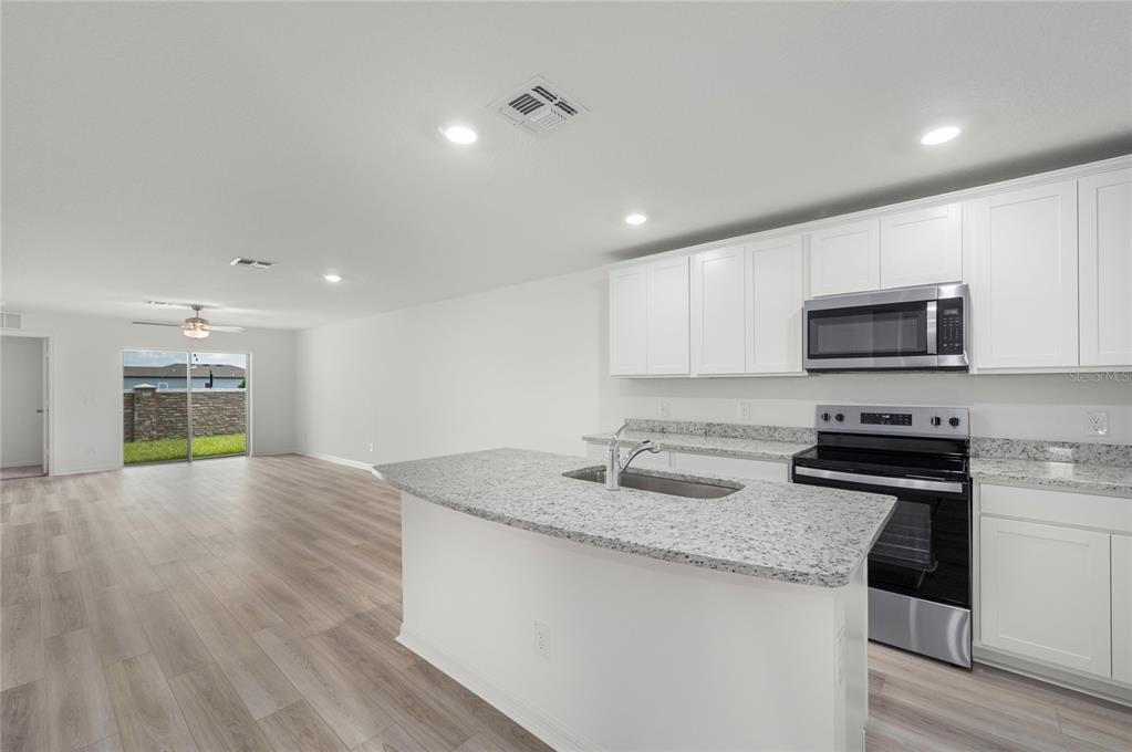 A kitchen with white cabinets, granite countertops, and an island overlooks an open living area — 3187 SEVILLE STREET, LAKE ALFRED, FL