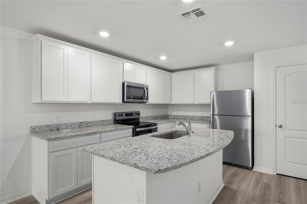 A kitchen features white cabinets, granite countertops, stainless steel appliances, and a central island — 3187 SEVILLE STREET, LAKE ALFRED, FL