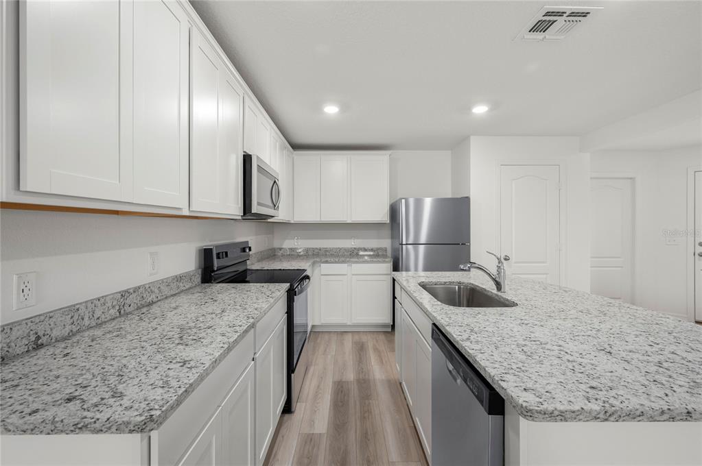 A kitchen features white cabinets, granite countertops, stainless steel appliances, and light wood-look flooring — 3187 SEVILLE STREET, LAKE ALFRED, FL