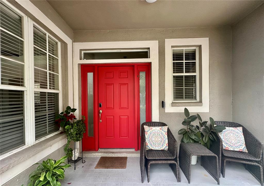 A front porch features a bright red door, two wicker chairs, and potted plants — 12014 DEACONS CROFT LANE, TAMPA, FL