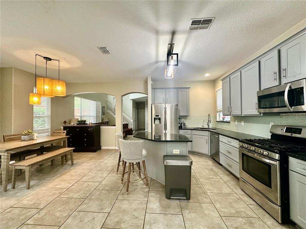 A kitchen features light gray cabinets, stainless steel appliances, a center island, and tile flooring — 12014 DEACONS CROFT LANE, TAMPA, FL