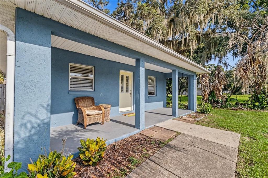 A blue house exterior features a covered front porch, a wicker chair, and concrete walkway — 156 GAINES STREET, OAK HILL, FL