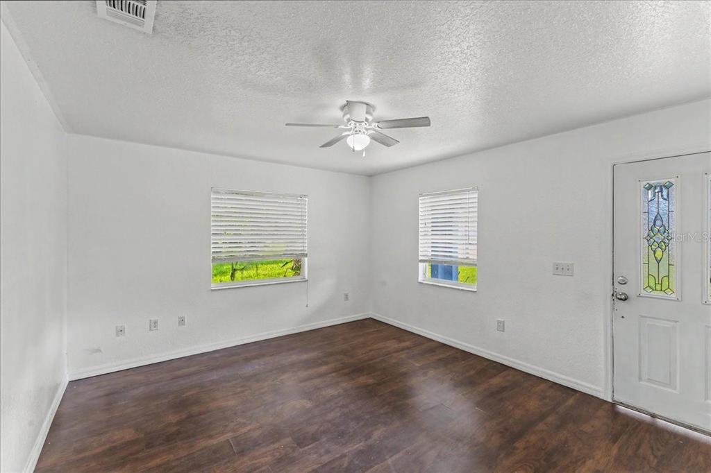 An empty room with white walls, dark wood-look flooring, two windows, and a ceiling fan — 156 GAINES STREET, OAK HILL, FL
