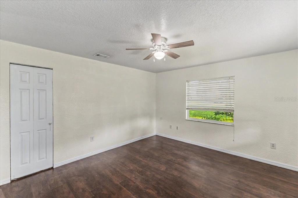 An empty bedroom features white walls, dark wood-look flooring, a ceiling fan, and a window — 156 GAINES STREET, OAK HILL, FL