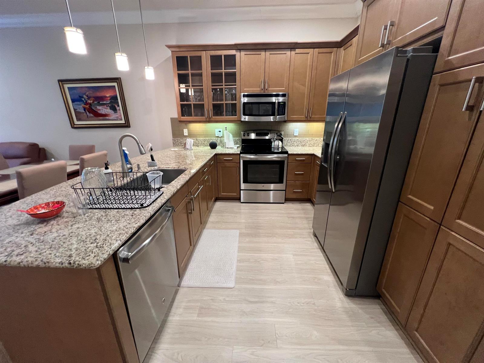 A kitchen features wood cabinets, stainless steel appliances, granite countertops, and light-colored wood flooring — 14856 Barletta Way, Delray Beach FL 33446, DELRAY BEACH, FL