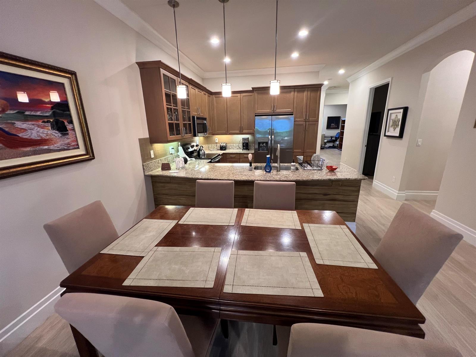 A dining area with a wooden table and chairs sits before an open-concept kitchen — 14856 Barletta Way, Delray Beach FL 33446, DELRAY BEACH, FL