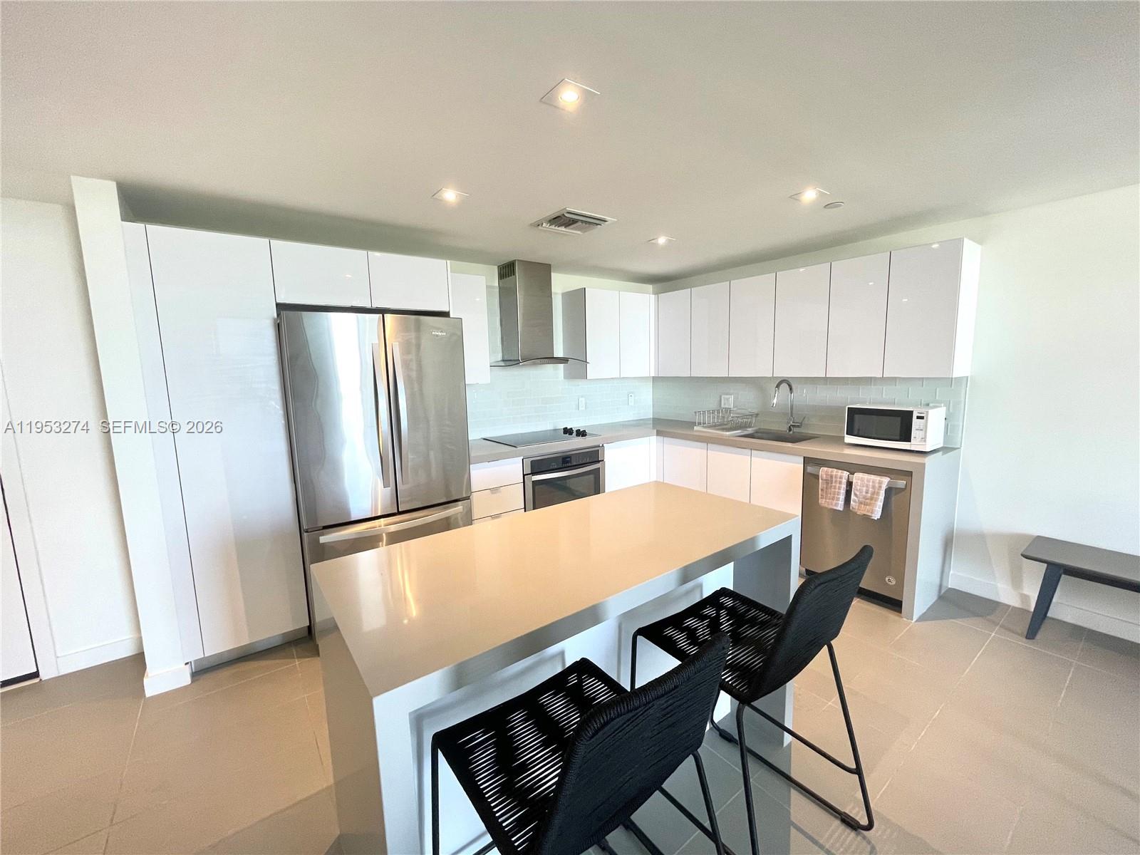 A modern kitchen features white cabinets, stainless steel appliances, and a central island with stools — 1600 NE 1st Ave # 1018, Miami FL 33132, MIAMI, FL