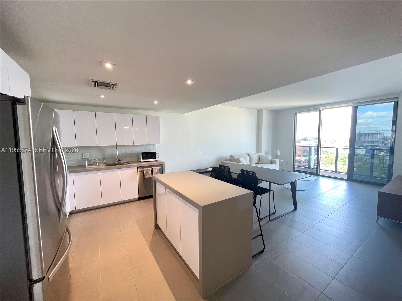 A modern kitchen with white cabinetry and a central island opens into a living area — 1600 NE 1st Ave # 1018, Miami FL 33132, MIAMI, FL