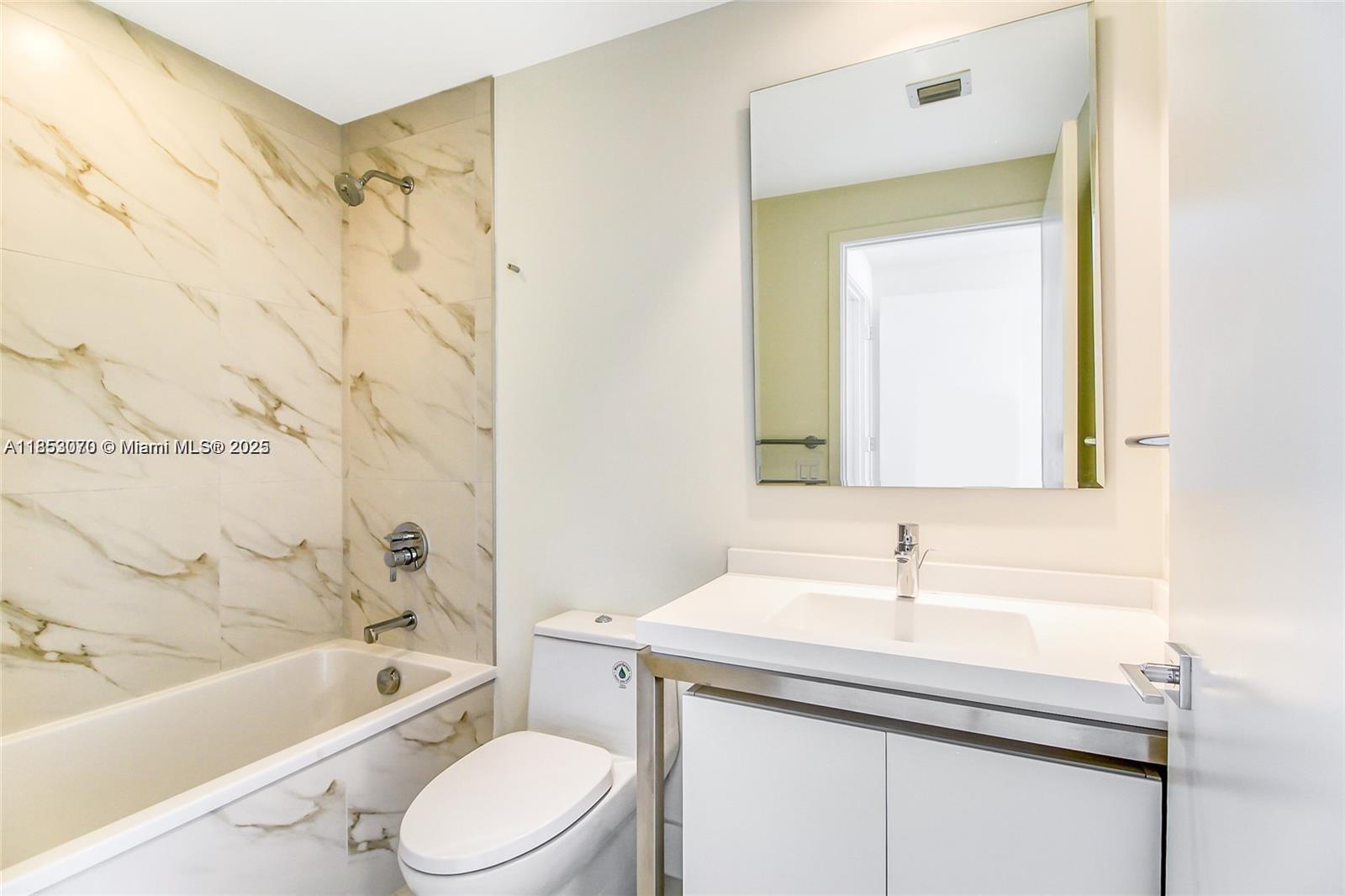 A bathroom features a marble-tiled bathtub, a white toilet, and a modern vanity with mirror — 2000 Metropica Way # 1709, Sunrise FL 33323, SUNRISE, FL
