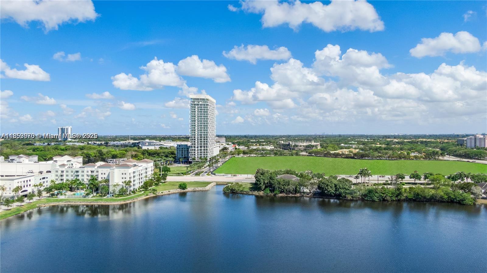 An aerial view shows a lake in the foreground, a large apartment complex, and a high-rise — 2000 Metropica Way # 1709, Sunrise FL 33323, SUNRISE, FL