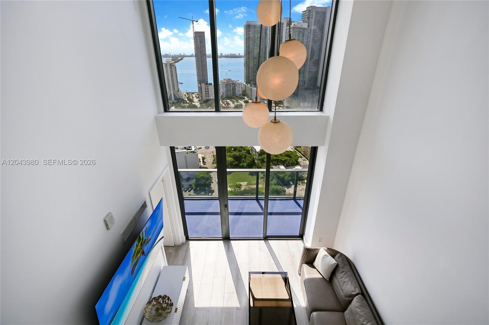 A high-ceiling living room features a large window wall, a chandelier, and a balcony — 121 NE 34th St, Miami FL 33137, MIAMI, FL