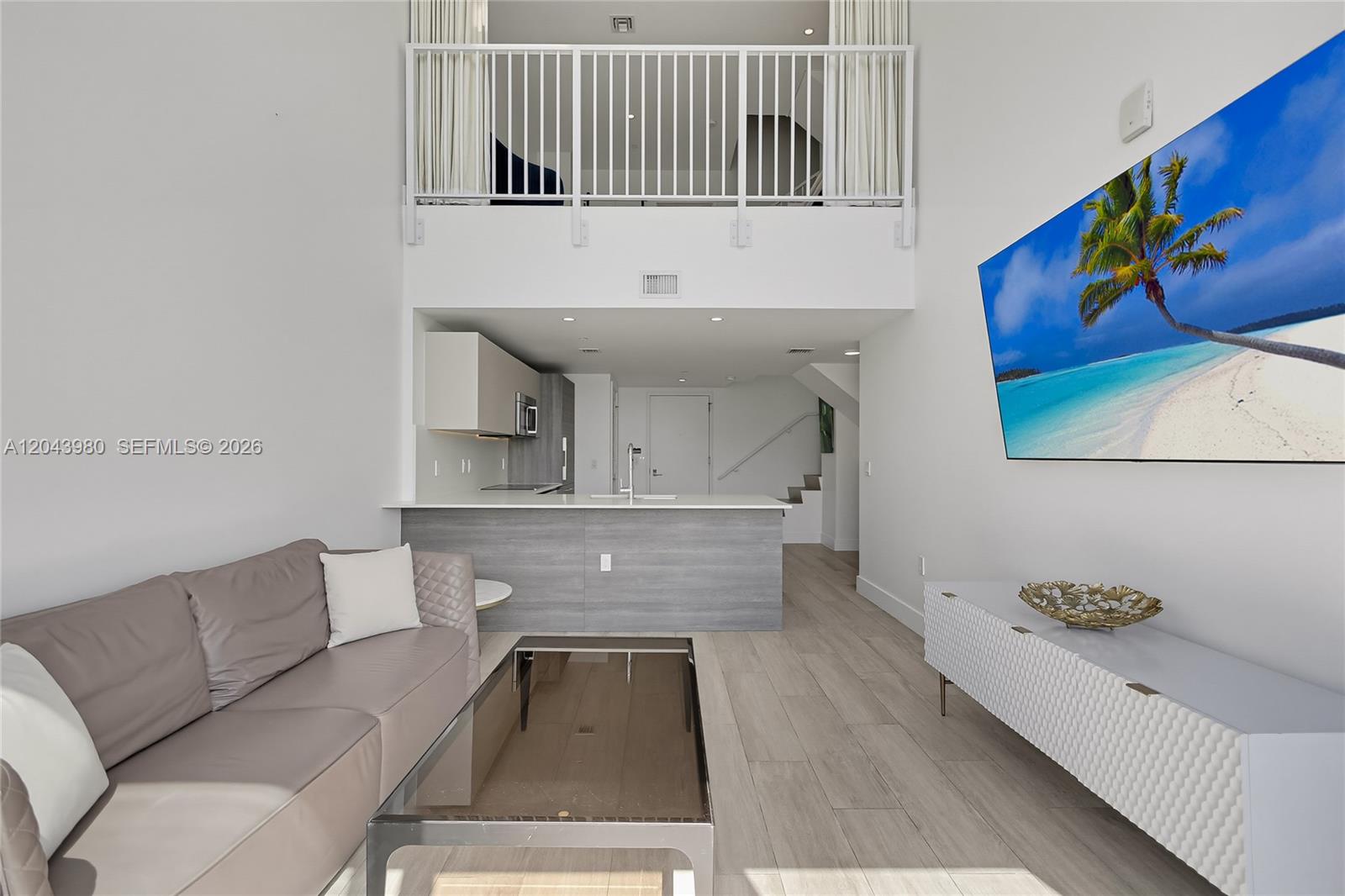 A modern living room features a lofted balcony, an open kitchen, and a wall-mounted television — 121 NE 34th St, Miami FL 33137, MIAMI, FL