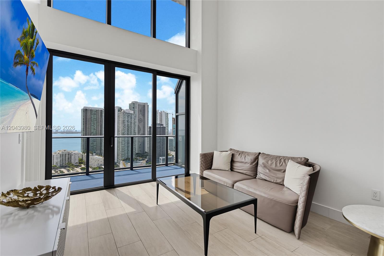 A modern living room features floor-to-ceiling windows with city views and a leather sofa — 121 NE 34th St, Miami FL 33137, MIAMI, FL
