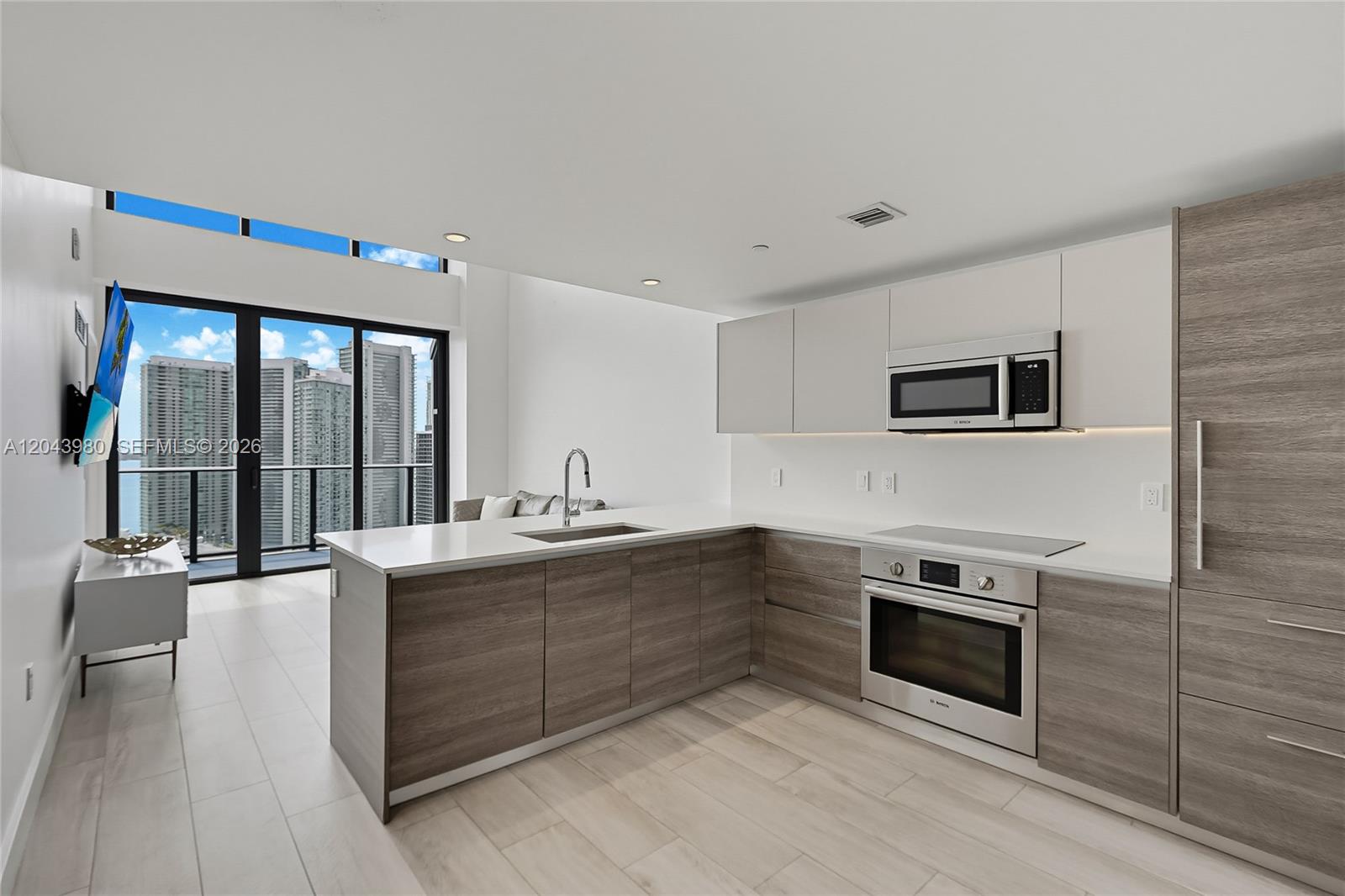 A modern kitchen features wood-grain cabinetry, white countertops, and floor-to-ceiling windows with city views — 121 NE 34th St, Miami FL 33137, MIAMI, FL