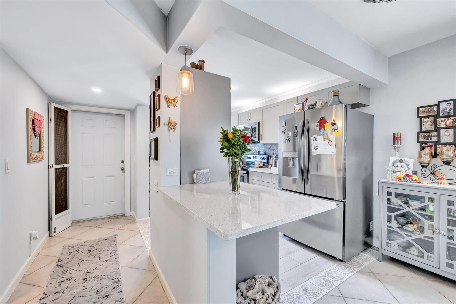 A kitchen with a peninsula, stainless steel refrigerator, and light-colored cabinetry opens to an entryway — 305 Congressional Way, Deerfield Beach FL 33442, DEERFIELD BEACH, FL