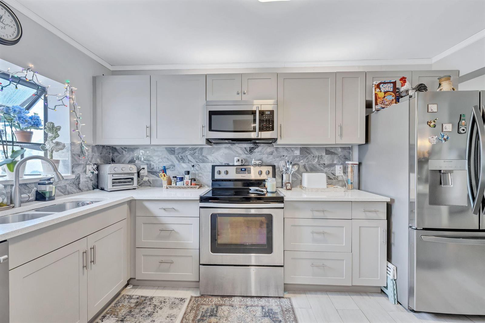 A kitchen featuring gray cabinets, stainless steel appliances, a marble-patterned backsplash, and white countertops — 305 Congressional Way, Deerfield Beach FL 33442, DEERFIELD BEACH, FL