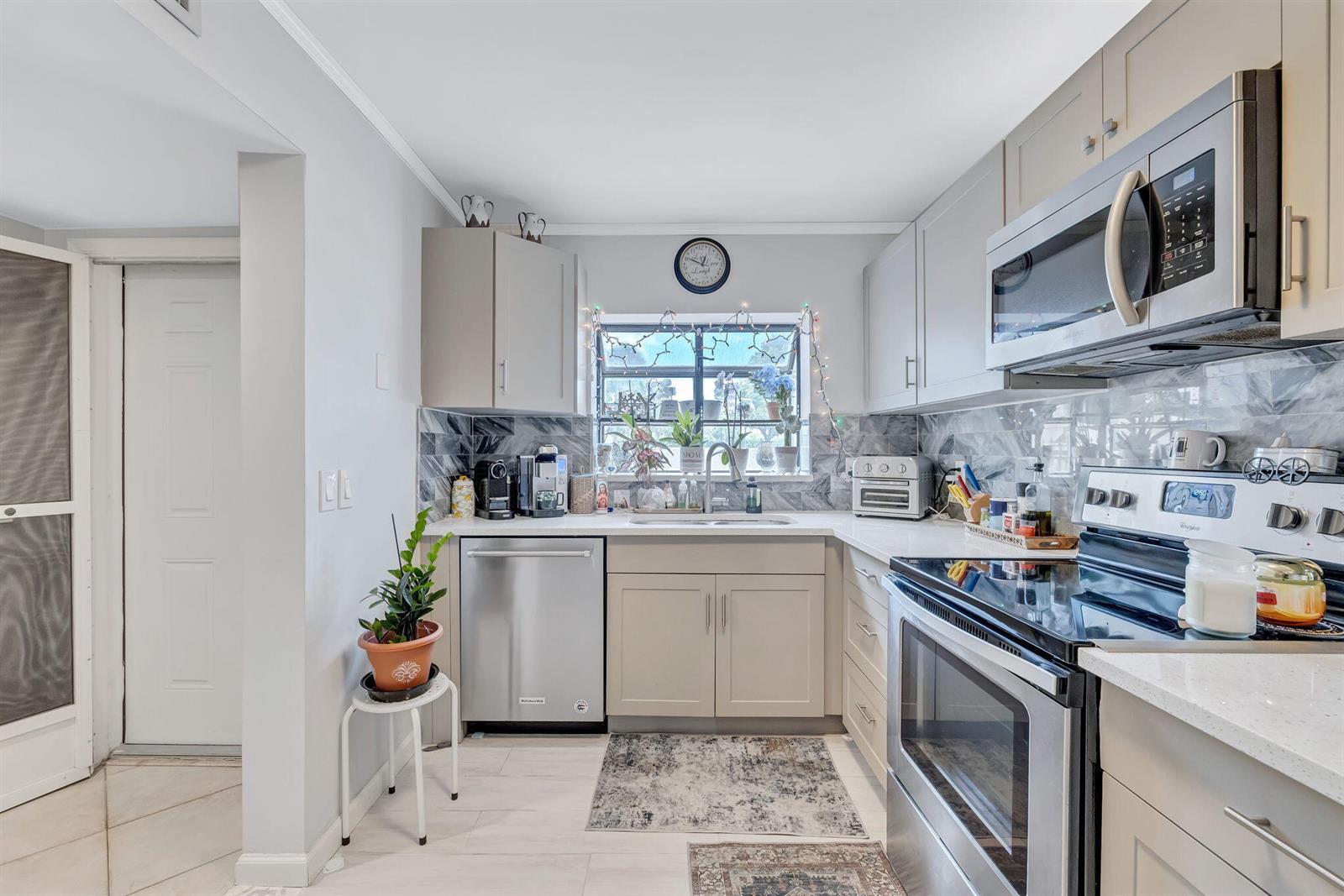 A kitchen features light gray cabinets, stainless steel appliances, a window, and a marble backsplash — 305 Congressional Way, Deerfield Beach FL 33442, DEERFIELD BEACH, FL