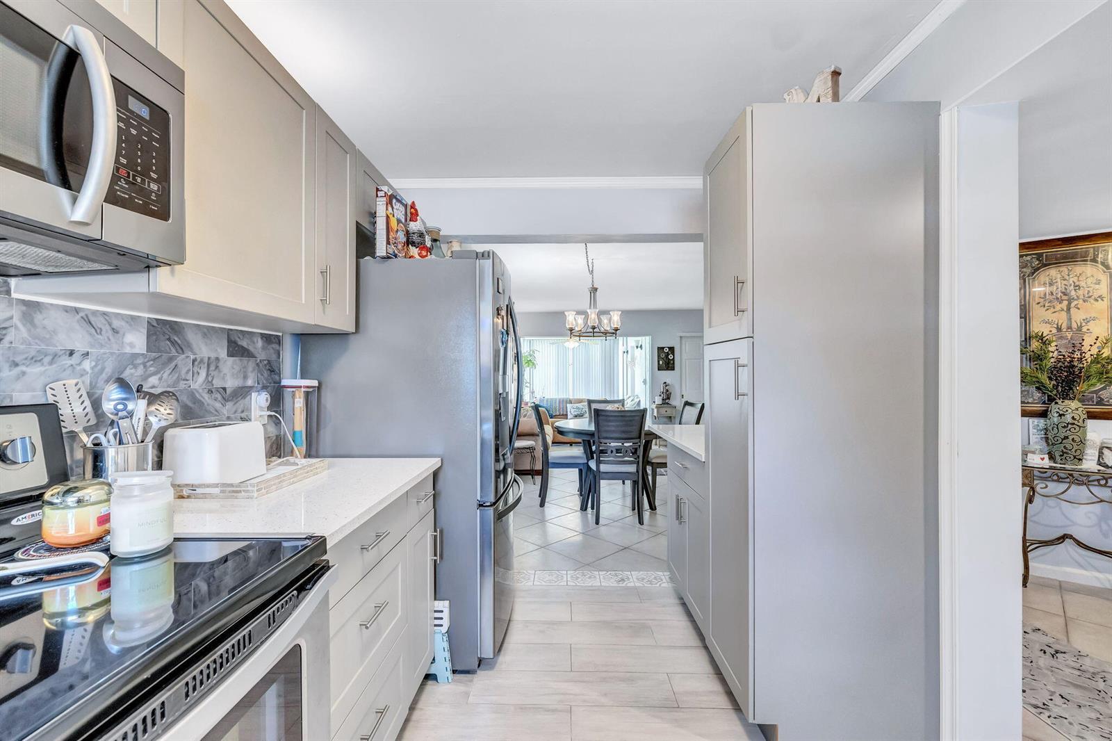 A kitchen with grey cabinets, stainless steel appliances, and quartz countertops leads into a dining area — 305 Congressional Way, Deerfield Beach FL 33442, DEERFIELD BEACH, FL