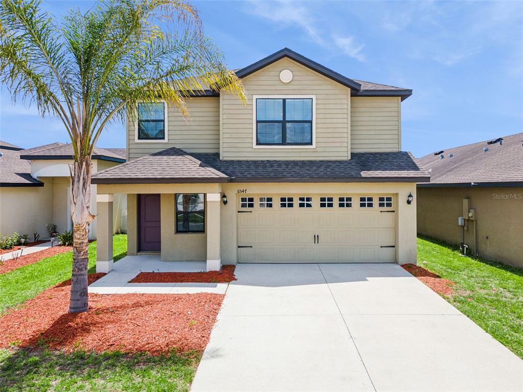 A two-story house with tan siding, a two-car garage, and a palm tree in front — 6547 BAIKAL PLACE, LAKELAND, FL